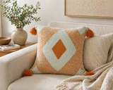 Orange and cream geometric tufted throw pillow with tassels styled on a neutral sofa in a modern living room