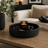 Matte black decorative tray styled as a candle centerpiece with beads and decor on a modern living room table with greenery and neutral furniture