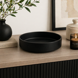 Matte black round decorative tray styled on a modern wood console with vase, books, candle, and minimalist home decor accents