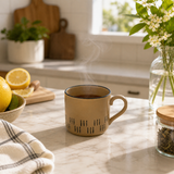 Brown ceramic mug with hot tea and steam on marble kitchen counter with lemons and flowers in bright natural light