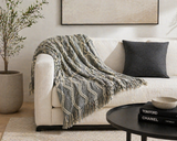 Gray textured throw blanket with tassels styled on a neutral sofa in a modern living room with minimalist decor