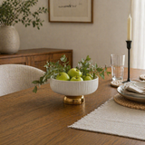 Modern dining table styled with a white ceramic bowl of green apples and greenery centerpiece, paired with neutral tableware and warm wood furniture for a cozy contemporary home setting