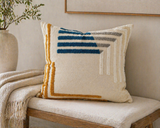 Modern textured throw pillow with geometric pattern in blue, gray, and mustard on a neutral upholstered bench with cozy home decor styling