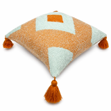 Side view of orange and cream geometric throw pillow with textured weave and tassel corners on a white background