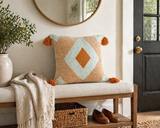 Orange and cream diamond tufted throw pillow with tassels styled on a wooden entryway bench with neutral decor and greenery