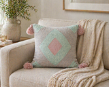Pastel geometric throw pillow with soft pink tassels styled on a neutral sofa with a cozy textured throw and warm natural decor