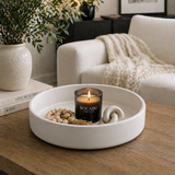 Matte white decorative tray styled with a candle, beads, and decor on a wooden table in a cozy modern living room with soft textiles and greenery