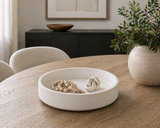 Matte white round decorative tray styled on a wooden dining table with neutral decor, beads, and modern minimalist home accessories