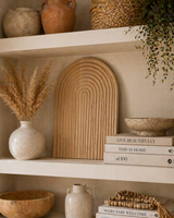 Wooden arched textured decorative tray styled on open shelves with ceramic vases, books, and natural decor in a warm boho home interior